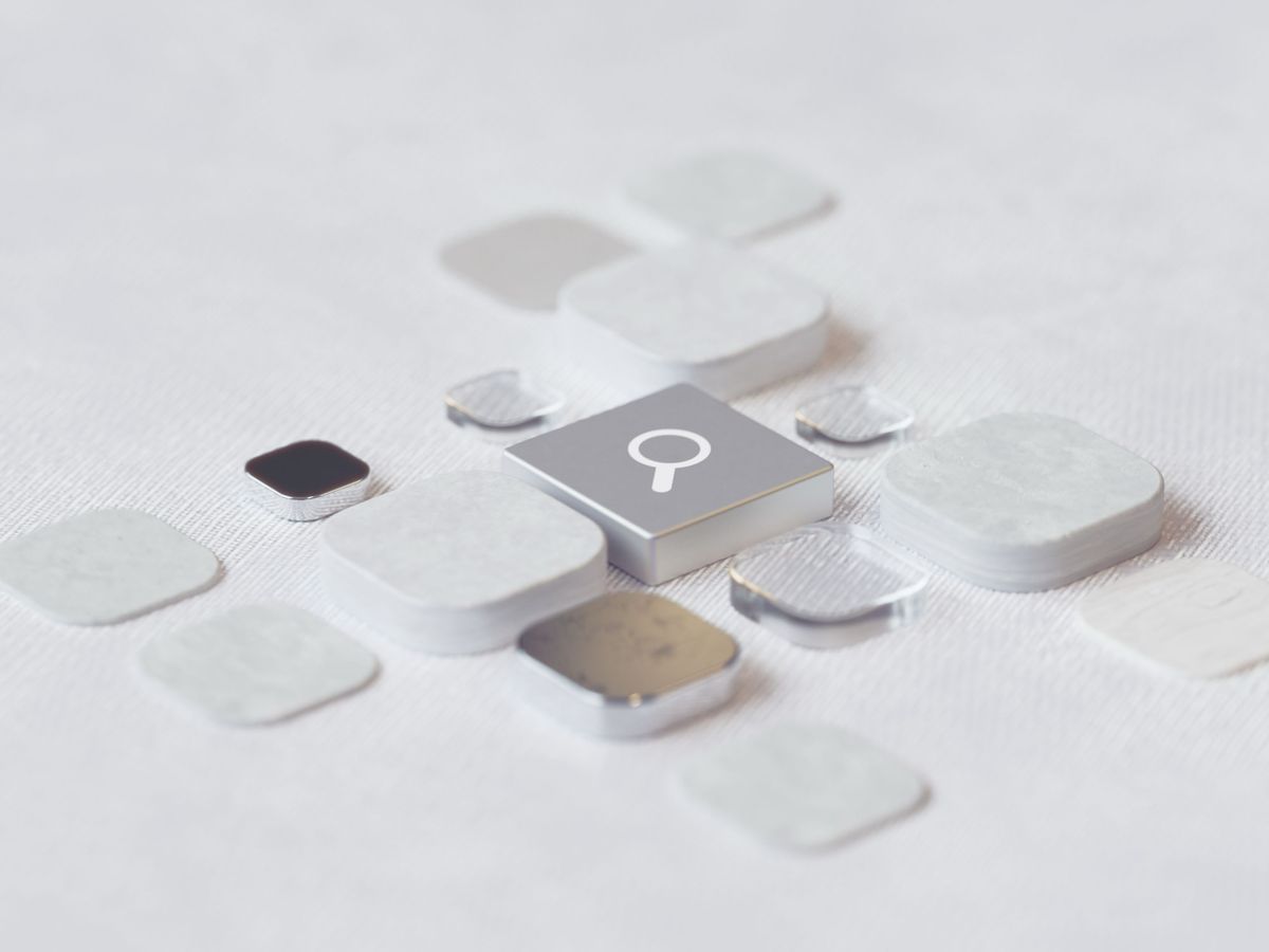 A metallic search-icon key at the center of a grid of blank white and silver app-style tiles on a textured surface