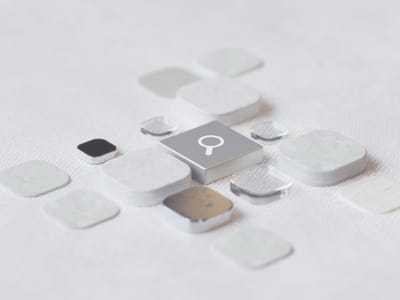 A metallic search-icon key at the center of a grid of blank white and silver app-style tiles on a textured surface